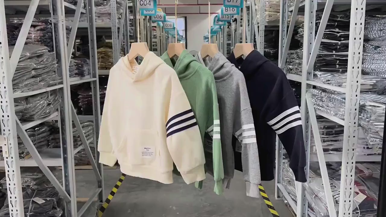 Kids' hooded sweatshirts in beige, gray, green, and navy blue with white stripes, fleece-lined for warmth, hanging in a warehouse.